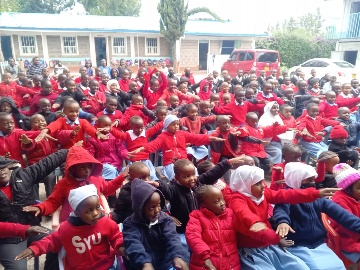 Schoolchildren in red uniforms raising their hands during an outreach in Kenya